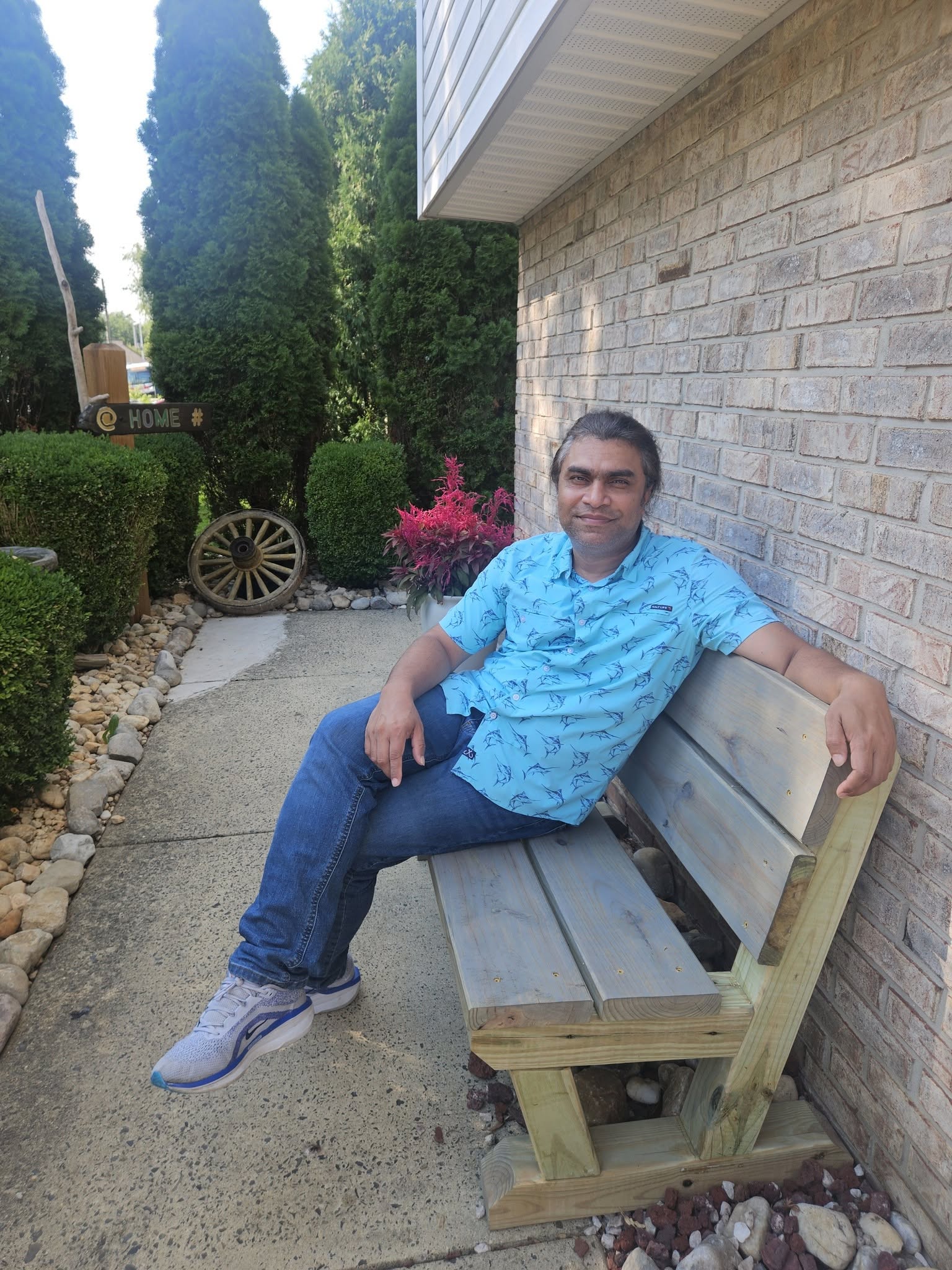 The finished, stained bench installed against the brick wall in the front yard garden