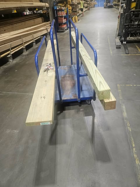 Cart loaded with long pressure-treated boards in the Lowe's aisle