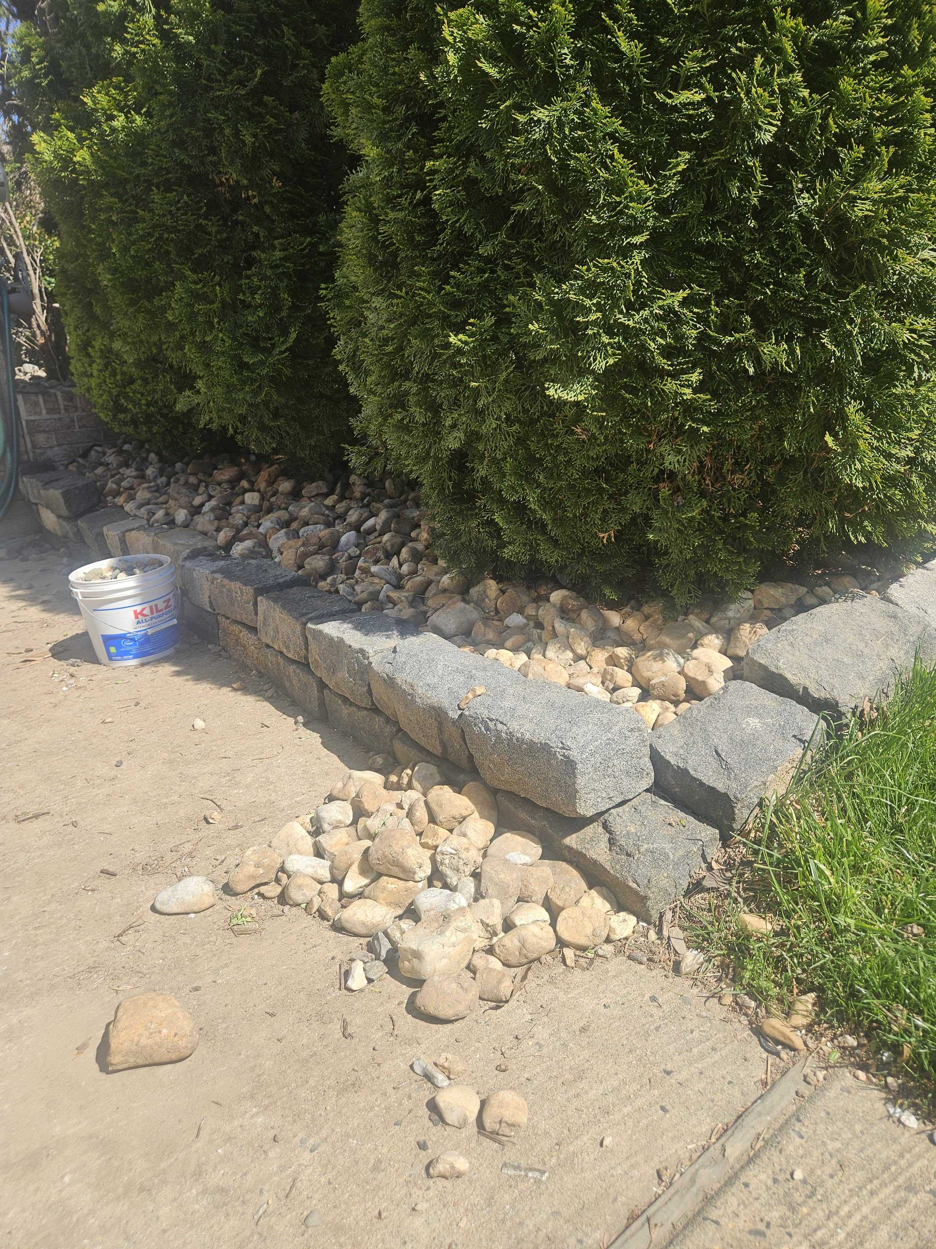 Belgian blocks being laid as a border along the front bed with rocks piled nearby