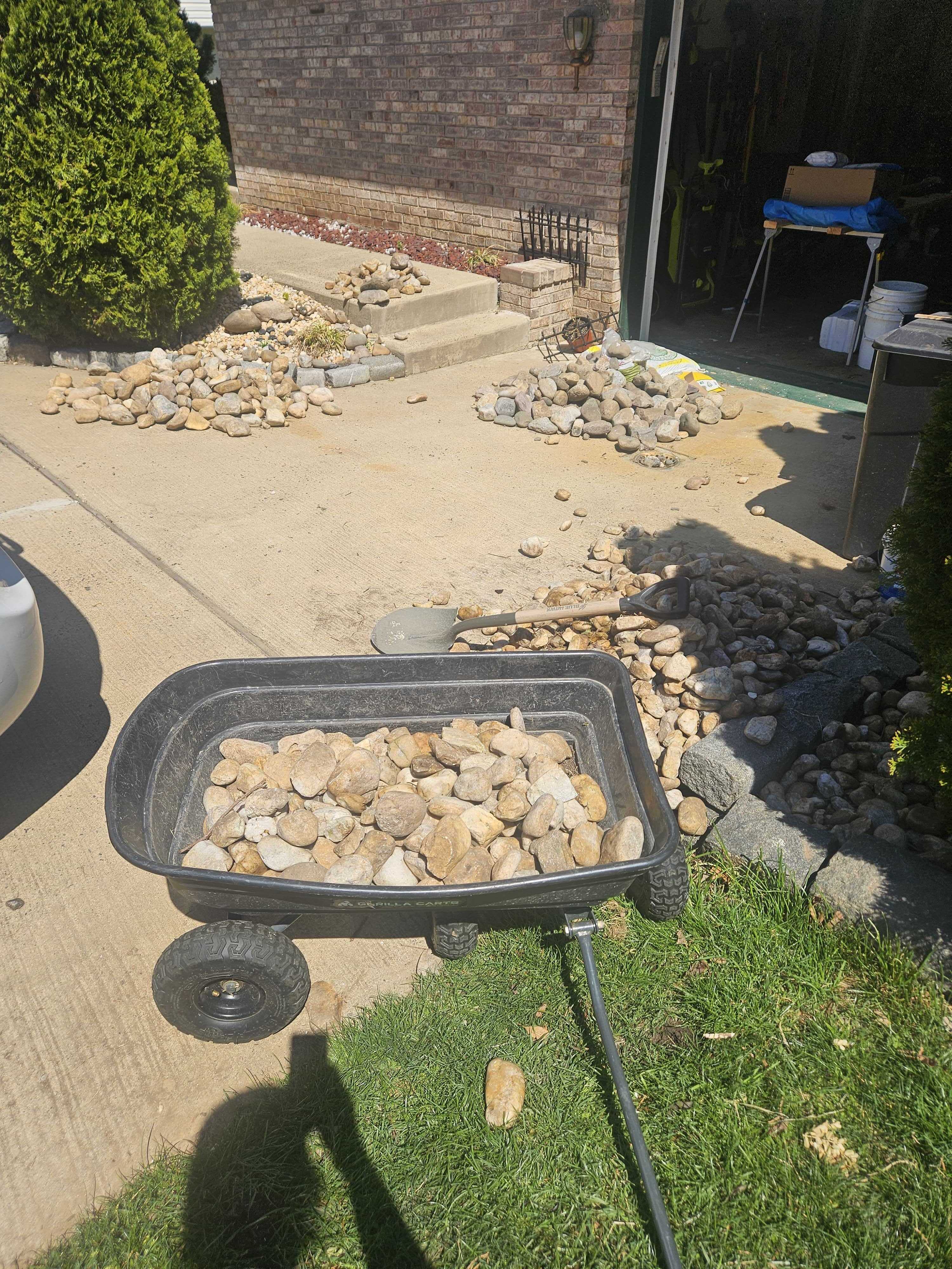 Garden wagon loaded with river rocks in the driveway, piles of rocks in the background
