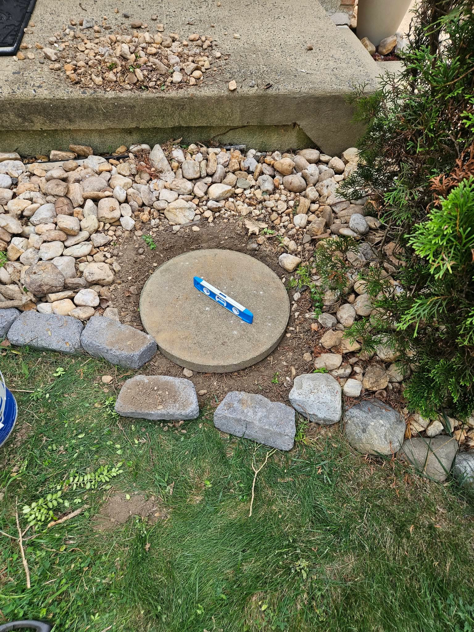 A round concrete stepping stone set into a dug-out spot in the front garden rock bed