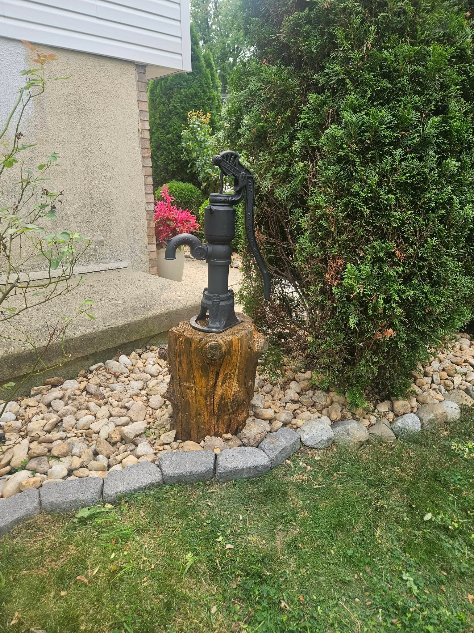 An old-style hand well pump mounted on top of the finished stump in the garden bed